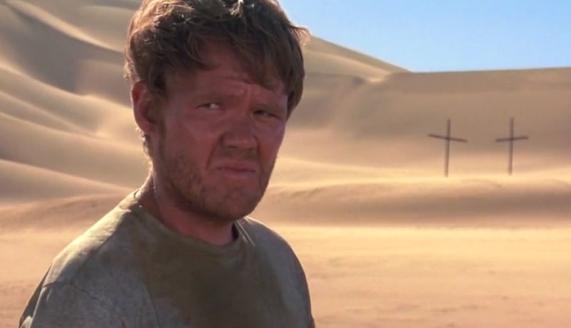 Liddle looking puzzled in the desert with two crosses in the background.