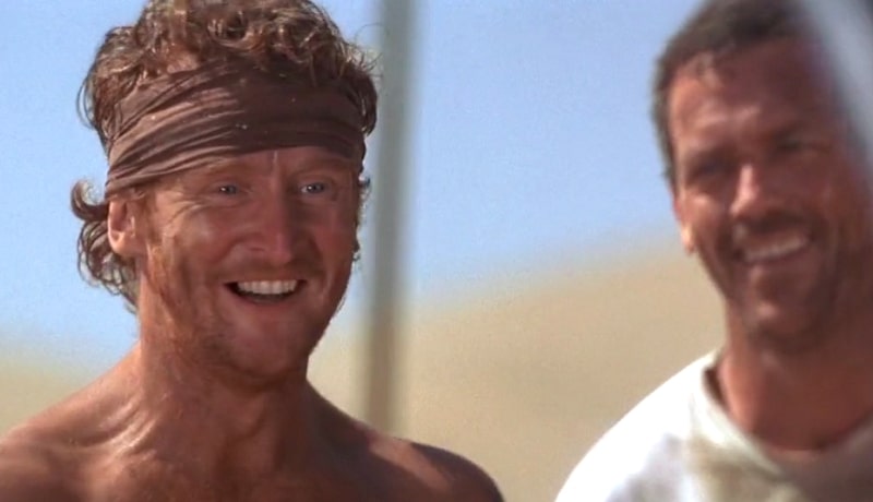 Rodney with a bandana smiling with Ian behind him in the desert.
