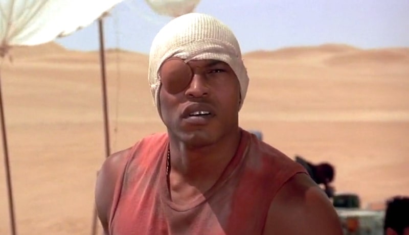 Sticky Fingaz with an eyepatch and white rag on his head looking confused in the desert.
