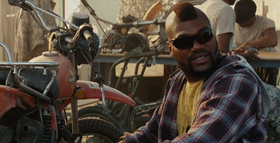 Quinton Rampage Jackson with a mohawk working on a motorcycle in the desert.