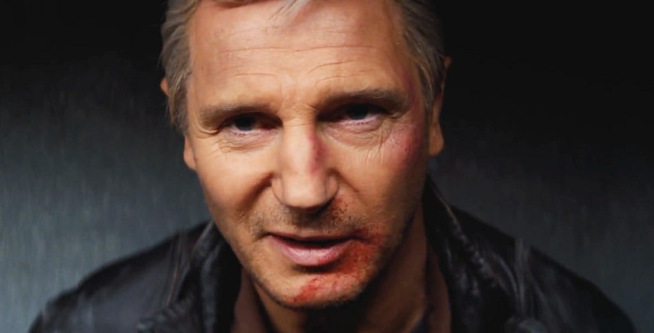 Liam Neeson as Hannibal in The A-Team with a smug smile in a dark room.