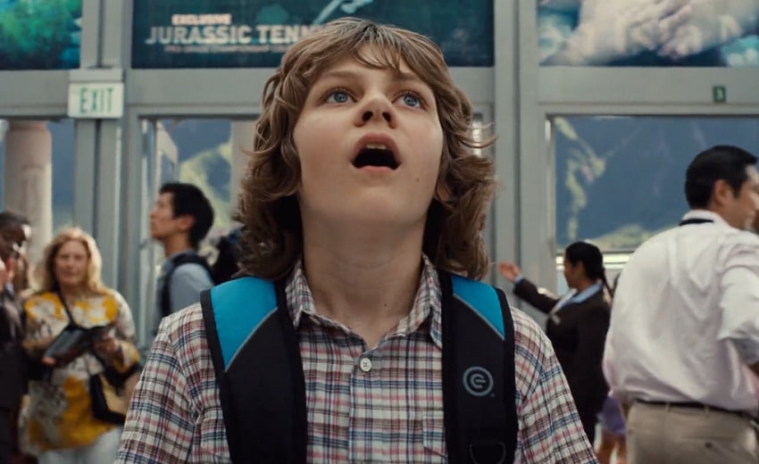 Young boy with brown hair and button-up shirt looking up in awe with his mouth wide open in Jurassic World.