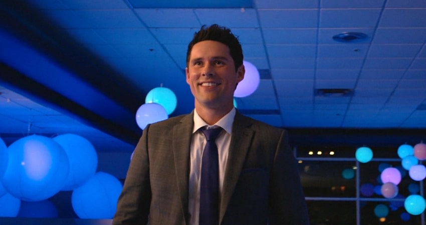 A young man in a suit smiling happily in a neon lighted room with ballons.