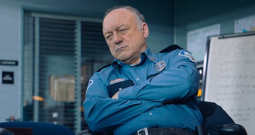 Old gray-haired police officer with his arms crossed in the office.