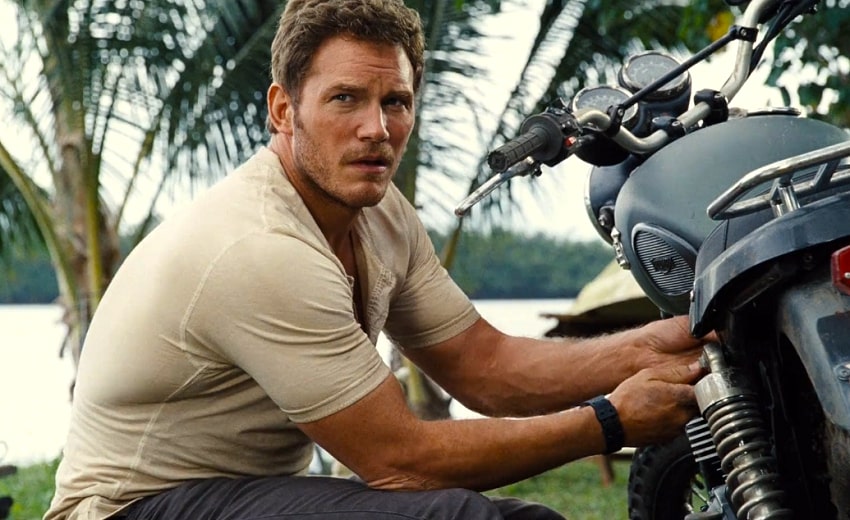 Owen Grady working on a motorcycle in a beige shirt looking over his shoulder in Jurassic World.